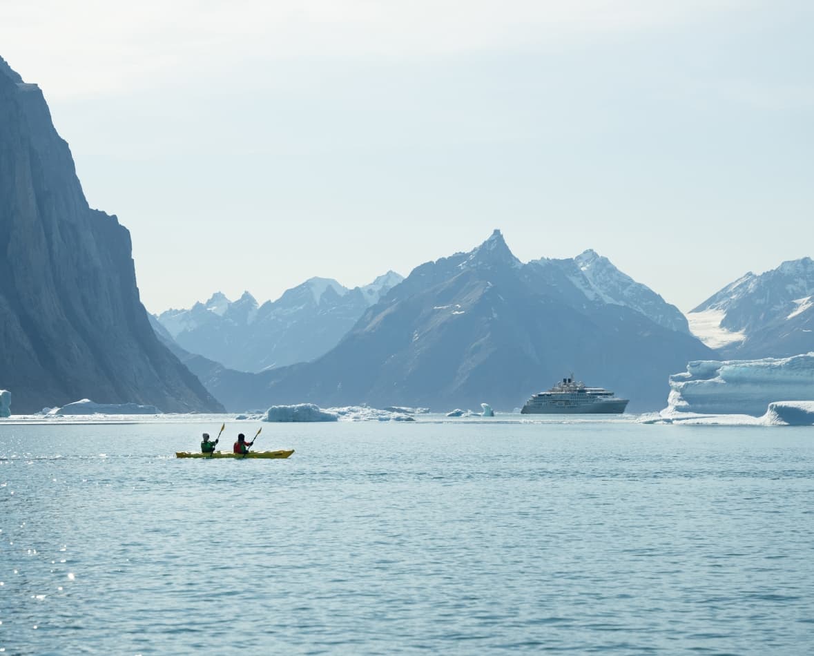 A pair of kayakers, with snowy and rocky cliffs in the background